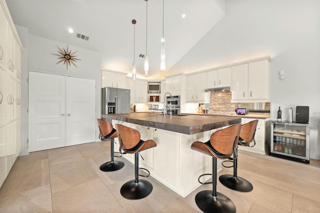 kitchen featuring pendant lighting, wine cooler, white cabinets, high vaulted ceiling, and appliances with stainless steel finishes