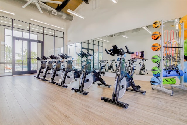 exercise room with ceiling fan, french doors, hardwood / wood-style floors, and a high ceiling