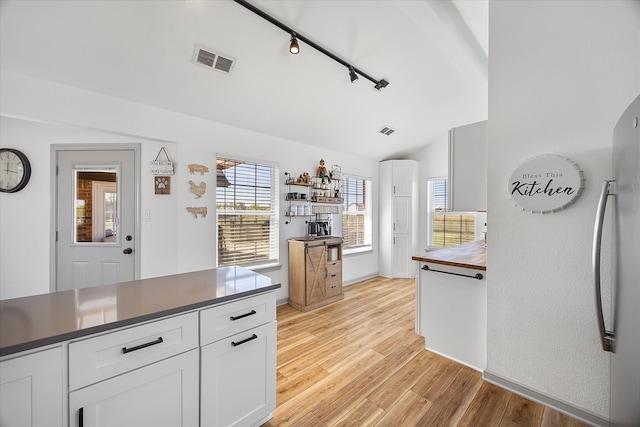 kitchen with stainless steel fridge, rail lighting, lofted ceiling, white cabinets, and light hardwood / wood-style flooring