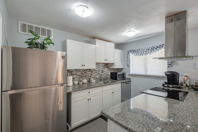 kitchen featuring dark stone countertops, white cabinetry, stainless steel appliances, sink, and wall chimney range hood