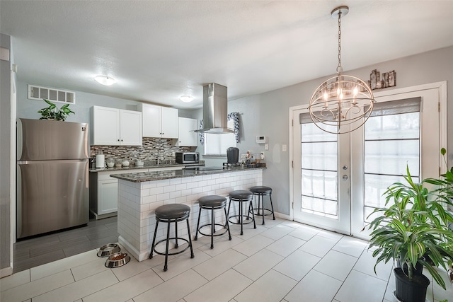 kitchen with kitchen peninsula, wall chimney exhaust hood, white cabinetry, stainless steel appliances, and a kitchen breakfast bar