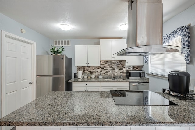 kitchen with sink, island exhaust hood, white cabinetry, appliances with stainless steel finishes, and dark stone counters