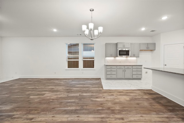 kitchen featuring gray cabinetry, dark wood-type flooring, hanging light fixtures, backsplash, and a chandelier