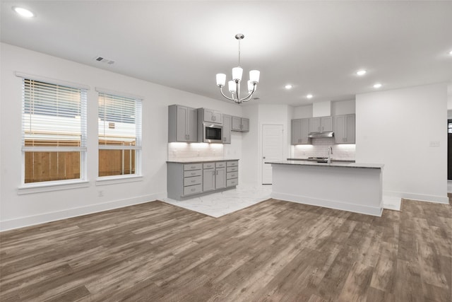 kitchen with stainless steel microwave, hanging light fixtures, dark hardwood / wood-style floors, gray cabinets, and a chandelier