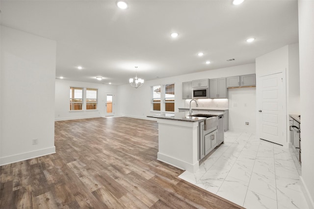 kitchen with built in microwave, sink, a chandelier, gray cabinets, and a center island with sink