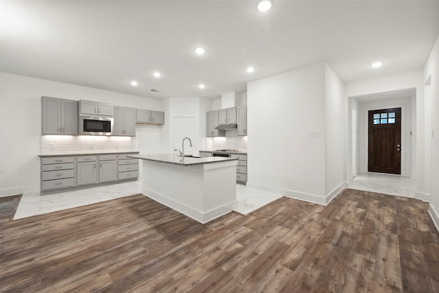 kitchen featuring backsplash, stainless steel gas cooktop, sink, gray cabinets, and an island with sink