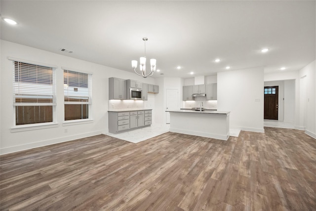 kitchen featuring dark hardwood / wood-style flooring, tasteful backsplash, stainless steel microwave, gray cabinets, and hanging light fixtures