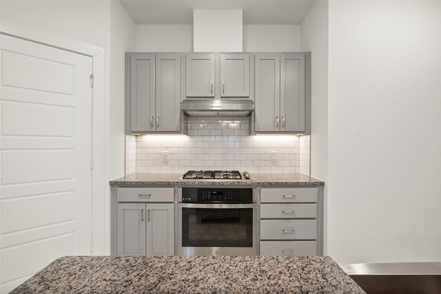 kitchen featuring gray cabinetry, light stone counters, stainless steel appliances, and tasteful backsplash