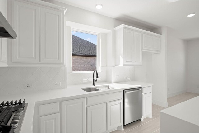 kitchen with white cabinetry, stainless steel dishwasher, wall chimney exhaust hood, and sink