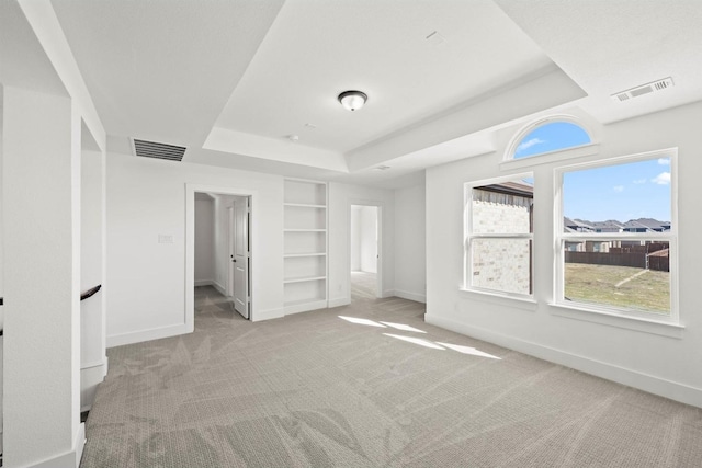 unfurnished bedroom featuring a raised ceiling, a walk in closet, and light colored carpet