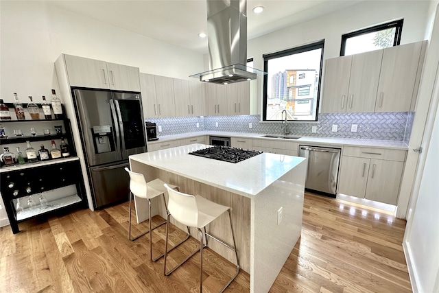 kitchen with a kitchen island, island exhaust hood, appliances with stainless steel finishes, a kitchen breakfast bar, and light hardwood / wood-style floors