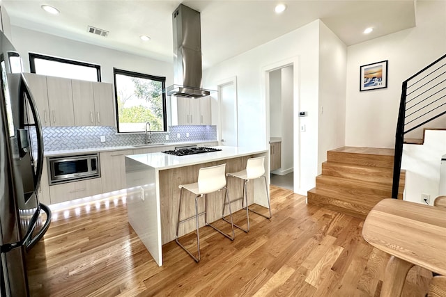 kitchen with appliances with stainless steel finishes, light hardwood / wood-style floors, tasteful backsplash, a center island, and range hood