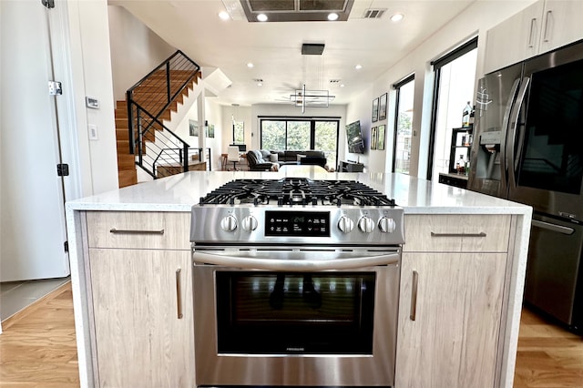 kitchen with light brown cabinets, stainless steel appliances, a center island, light stone countertops, and light hardwood / wood-style floors