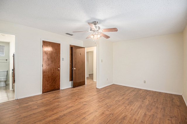 unfurnished bedroom featuring a textured ceiling, ensuite bath, light hardwood / wood-style flooring, and ceiling fan