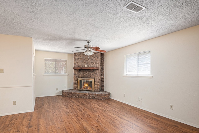 unfurnished living room with ceiling fan, a textured ceiling, a brick fireplace, and hardwood / wood-style floors