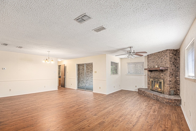 unfurnished living room featuring ceiling fan with notable chandelier, hardwood / wood-style floors, a textured ceiling, and a fireplace