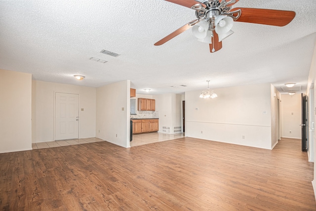 unfurnished living room with a textured ceiling, ceiling fan with notable chandelier, and light hardwood / wood-style flooring