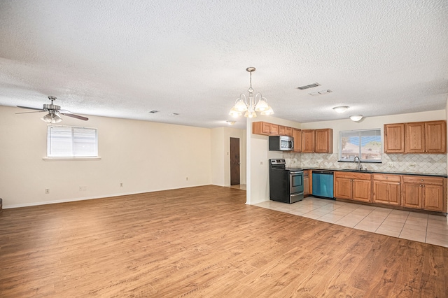 kitchen featuring ceiling fan with notable chandelier, light wood-type flooring, stainless steel appliances, and plenty of natural light