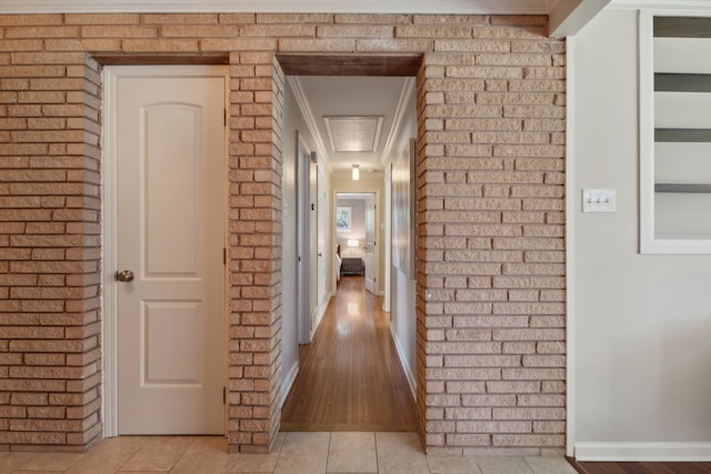 hall with light tile patterned flooring, brick wall, and ornamental molding