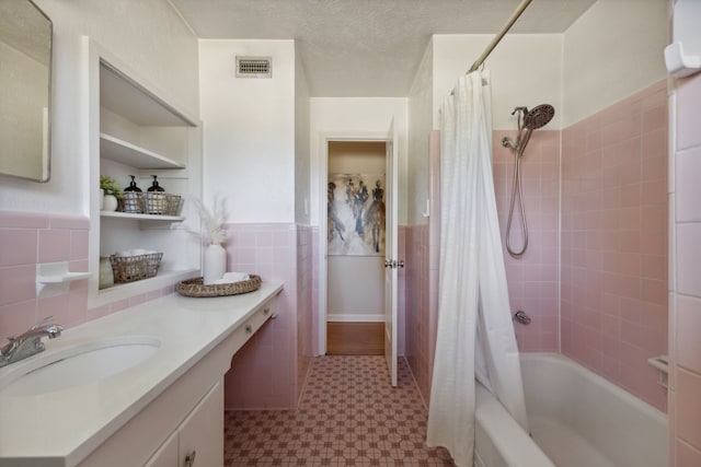 bathroom featuring a textured ceiling, shower / tub combo, vanity, and tile walls