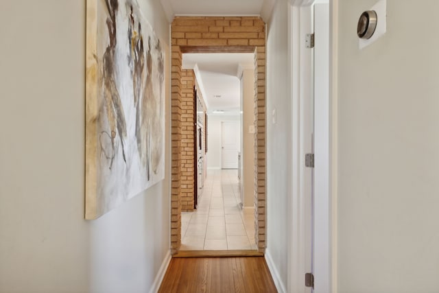 hall with light hardwood / wood-style floors and brick wall