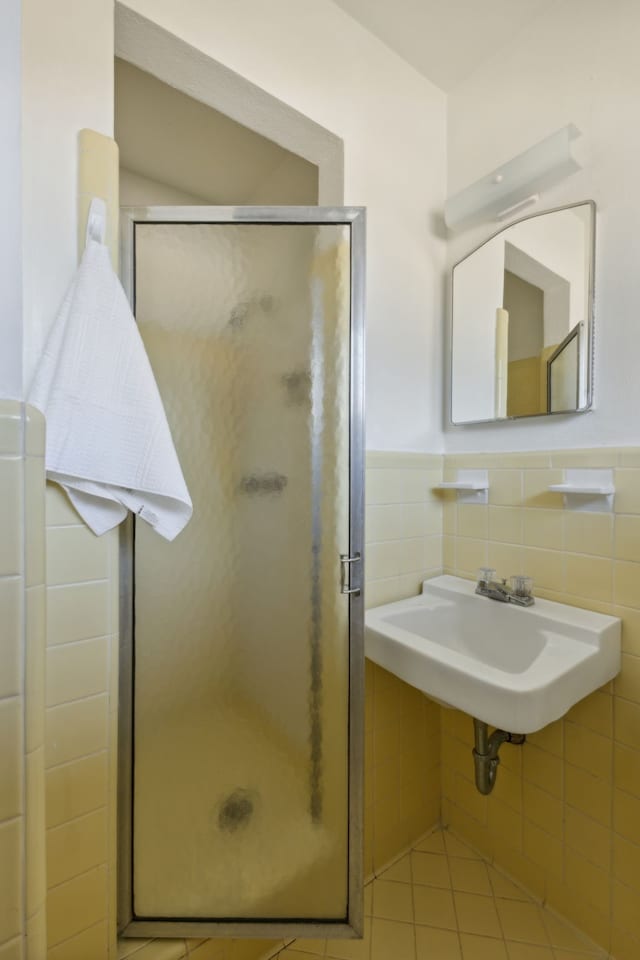 bathroom with tile patterned flooring, tile walls, a shower with shower door, and sink