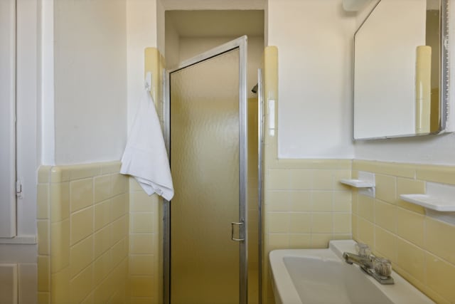 bathroom with sink, a shower with shower door, and tile walls