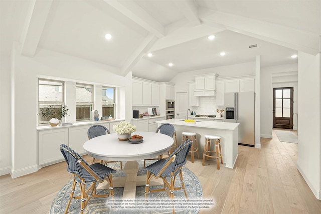 dining area with lofted ceiling with beams, sink, and light hardwood / wood-style flooring