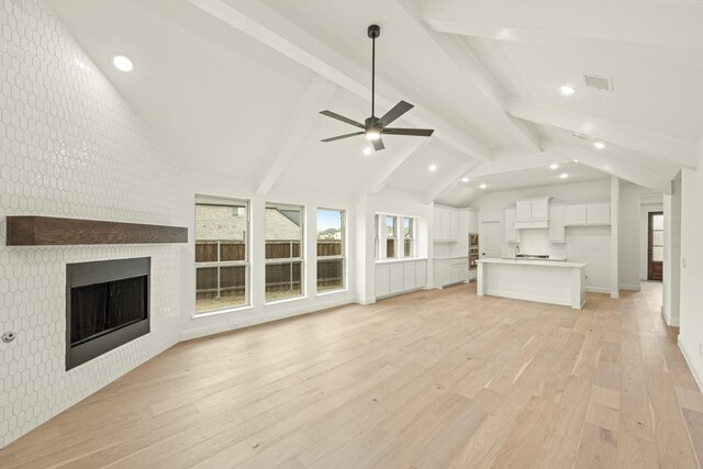 unfurnished living room with vaulted ceiling with beams, light hardwood / wood-style flooring, a brick fireplace, and ceiling fan