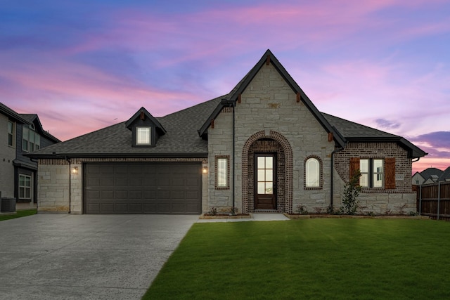 french country inspired facade featuring central AC unit, a garage, and a yard