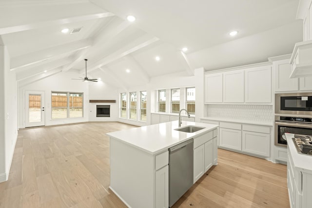 kitchen with sink, vaulted ceiling with beams, stainless steel appliances, a kitchen island with sink, and white cabinets