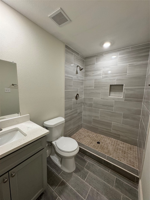 bathroom with vanity, toilet, and tiled shower