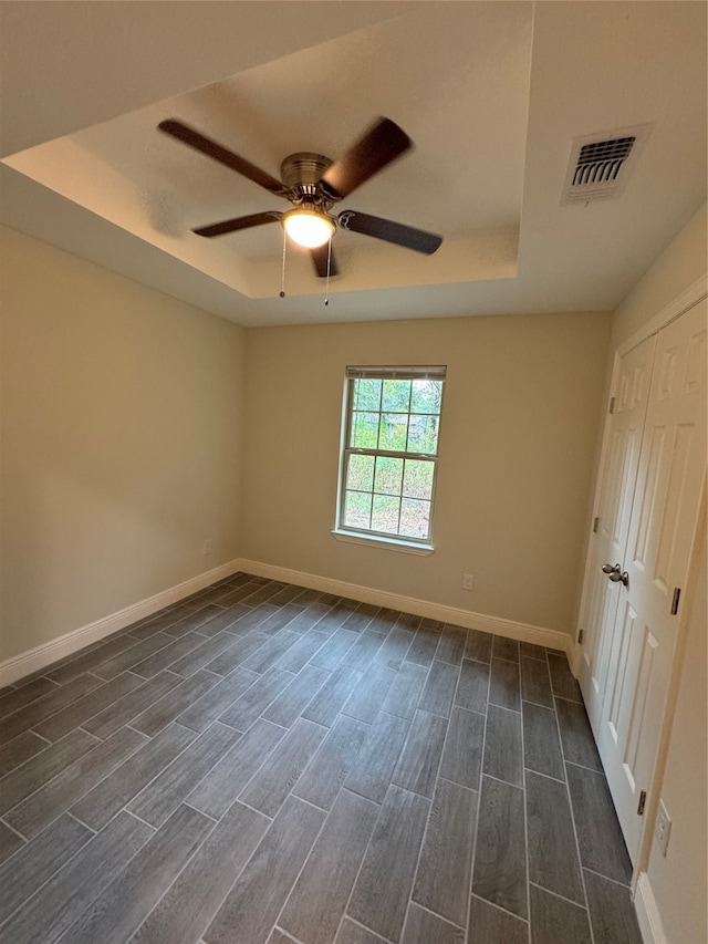 unfurnished bedroom featuring ceiling fan, a tray ceiling, and dark wood-type flooring