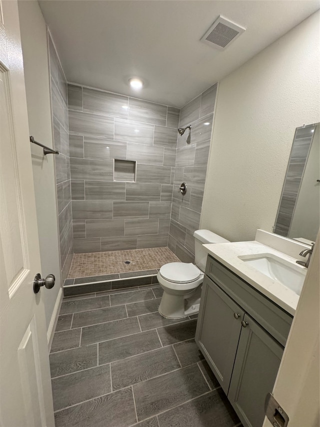 bathroom with a tile shower, vanity, and toilet