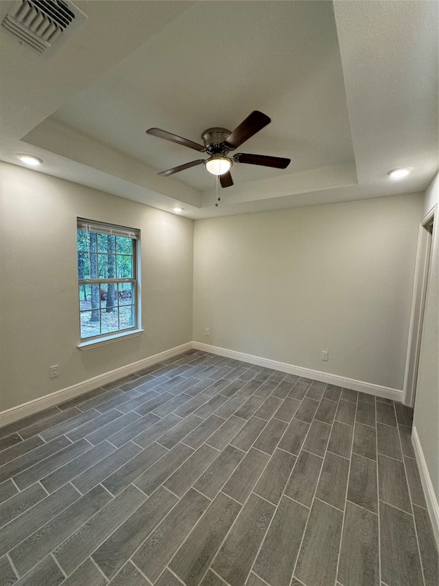 empty room with ceiling fan, a raised ceiling, and dark hardwood / wood-style flooring