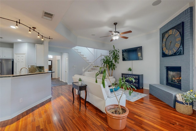 living room featuring dark wood-type flooring, sink, a brick fireplace, ornamental molding, and ceiling fan