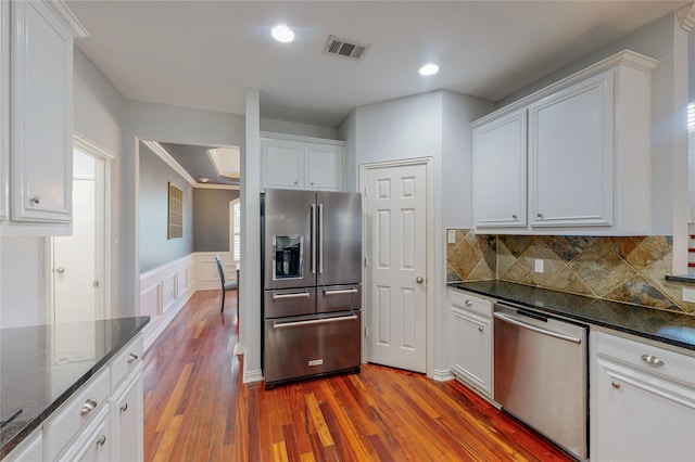 kitchen with dark stone countertops, appliances with stainless steel finishes, hardwood / wood-style floors, and white cabinetry