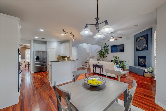 dining area featuring a brick fireplace, ceiling fan with notable chandelier, crown molding, dark hardwood / wood-style floors, and sink