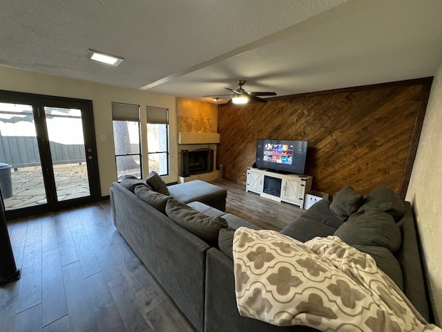 living room with a textured ceiling, dark hardwood / wood-style floors, a fireplace, wooden walls, and ceiling fan