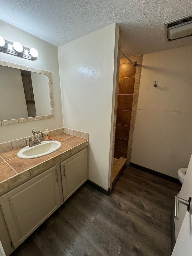 bathroom featuring a tile shower, hardwood / wood-style flooring, vanity, and toilet