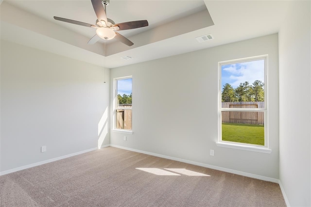 empty room with ceiling fan, a tray ceiling, and carpet