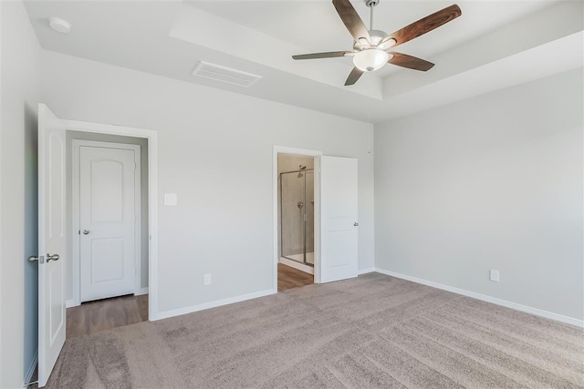 unfurnished bedroom with ensuite bathroom, carpet floors, ceiling fan, and a tray ceiling