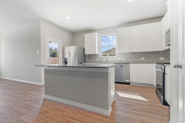 kitchen with stainless steel appliances, a center island, dark stone counters, and white cabinets