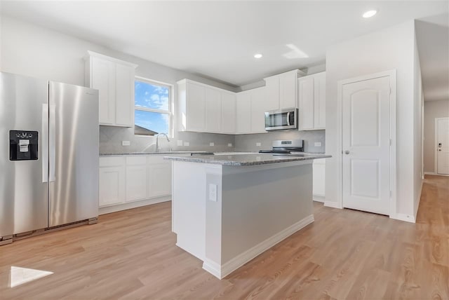 kitchen with white cabinetry, decorative backsplash, a center island, light stone counters, and stainless steel appliances