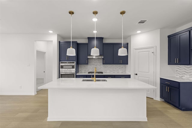 kitchen with blue cabinets, sink, stainless steel double oven, a kitchen island with sink, and backsplash