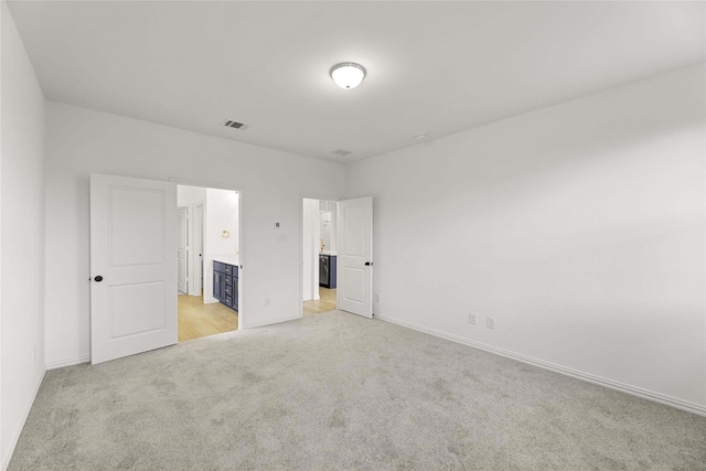 unfurnished bedroom featuring light colored carpet and connected bathroom