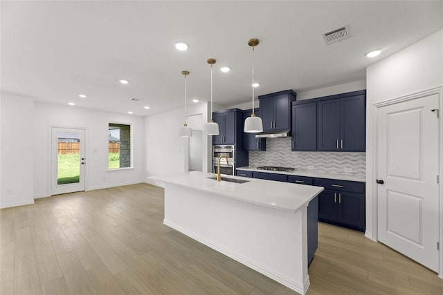 kitchen with appliances with stainless steel finishes, sink, backsplash, hanging light fixtures, and a kitchen island with sink