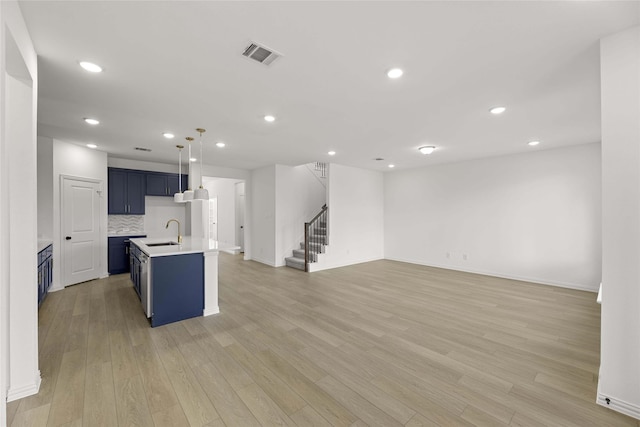 kitchen with blue cabinetry, sink, a center island with sink, light wood-type flooring, and decorative backsplash