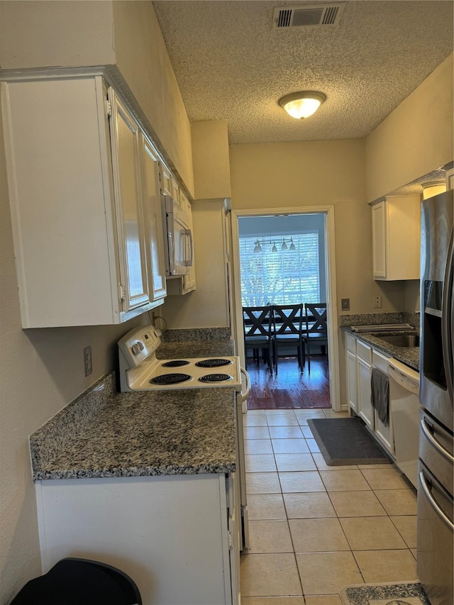 kitchen with white cabinets, dark stone counters, light tile patterned floors, white appliances, and a textured ceiling