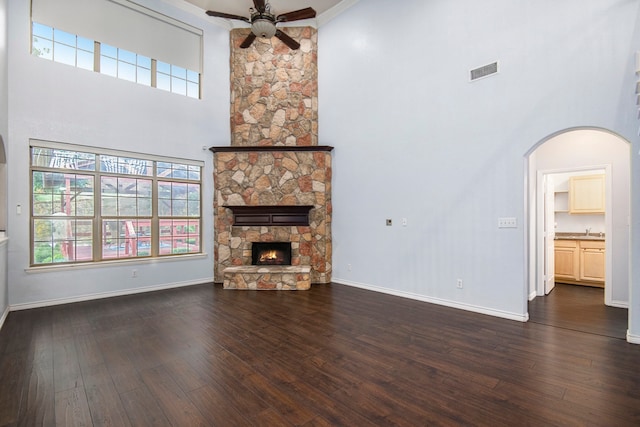 unfurnished living room with sink, a fireplace, a towering ceiling, dark hardwood / wood-style flooring, and ceiling fan